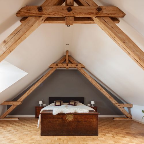 32309372 - interior of a loft or dormer bedroom in the apex of a roof with visible timber roof trusses , a patterned parquet floor and double bed